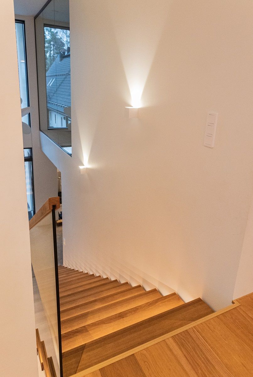 L'alta parete bianca della scala è illuminata da un punto luce nitido dell'applique FUNKit.